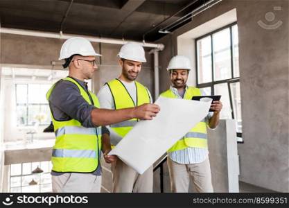 architecture, construction business and people concept - male architects in helmets with blueprint and tablet pc computer working in office building. architects with blueprint in office building