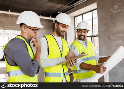 architecture, construction business and people concept - male architects in helmets with clipboard discussing blueprint in office building. architects in helmets with blueprint at office