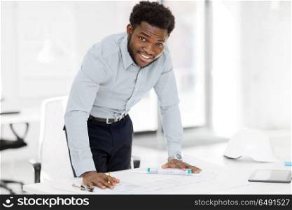 architecture, construction business and people concept - smiling african american architect with blueprint working at office. smiling african architect with blueprint at office. smiling african architect with blueprint at office