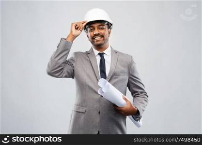 architecture, construction business and people concept - smiling indian male architect in helmet with blueprints over grey background. indian male architect in helmet with blueprints