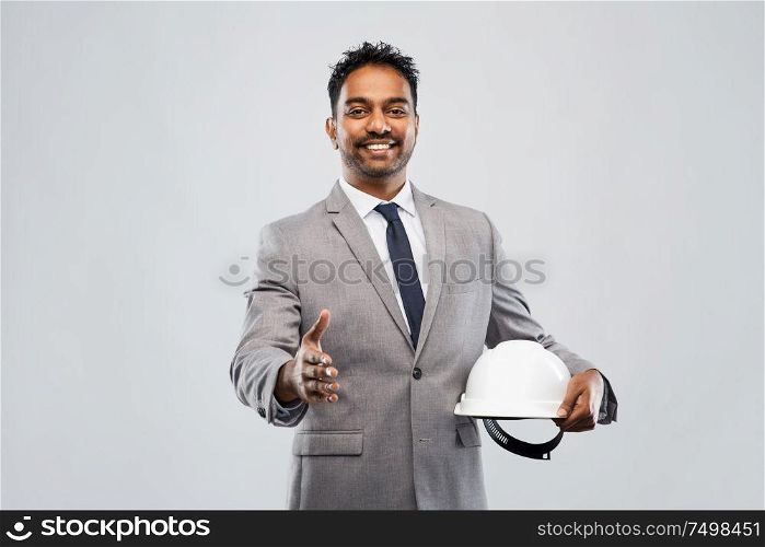 architecture, construction business and people concept - smiling indian male architect in helmet giving hand for handshake over grey background. male architect in helmet giving hand for handshake
