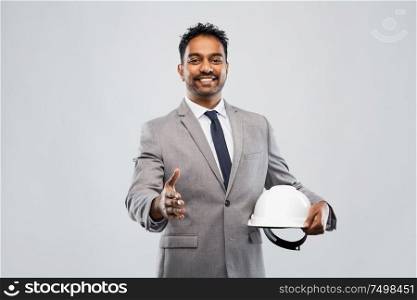 architecture, construction business and people concept - smiling indian male architect in helmet giving hand for handshake over grey background. male architect in helmet giving hand for handshake