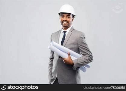 architecture, construction business and people concept - smiling indian male architect in helmet with blueprints over grey background. indian male architect in helmet with blueprints
