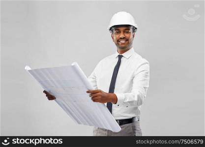 architecture, construction business and people concept - smiling indian male architect in helmet with blueprint over grey background. indian male architect in helmet with blueprint