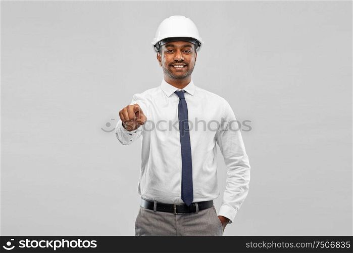 architecture, construction business and people concept - smiling indian male architect in helmet pointing finger to something over grey background. indian male architect in helmet showing something