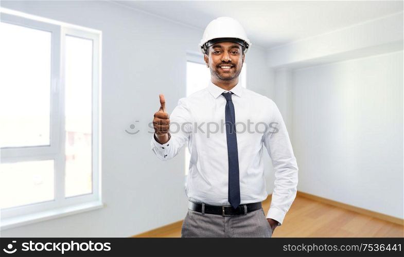 architecture, construction business and people concept - smiling indian male architect in helmet showing thumbs up over empty new apartment room background. indian male architect in helmet showing thumbs up