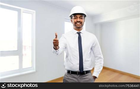 architecture, construction business and people concept - smiling indian male architect in helmet showing thumbs up over empty new apartment room background. indian male architect in helmet showing thumbs up