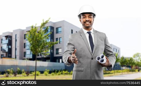 architecture, construction business and people concept - smiling indian male architect in helmet with blueprints giving hand for handshake over living houses on city street background. architect giving hand for handshake on city street