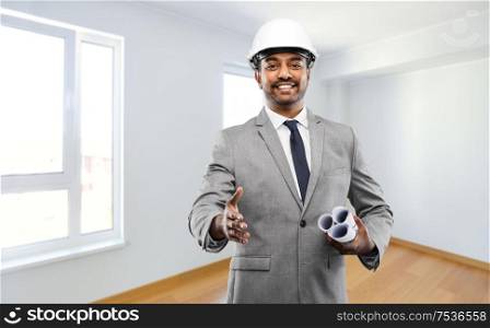 architecture, construction business and people concept - smiling indian male architect in helmet with blueprints giving hand for handshake over empty new apartment room background. male architect in helmet giving hand for handshake