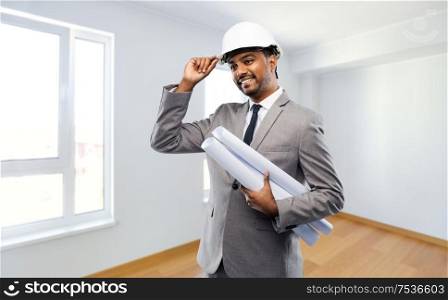 architecture, construction business and people concept - smiling indian male architect in helmet with blueprints over empty new apartment room background. indian male architect in helmet with blueprints