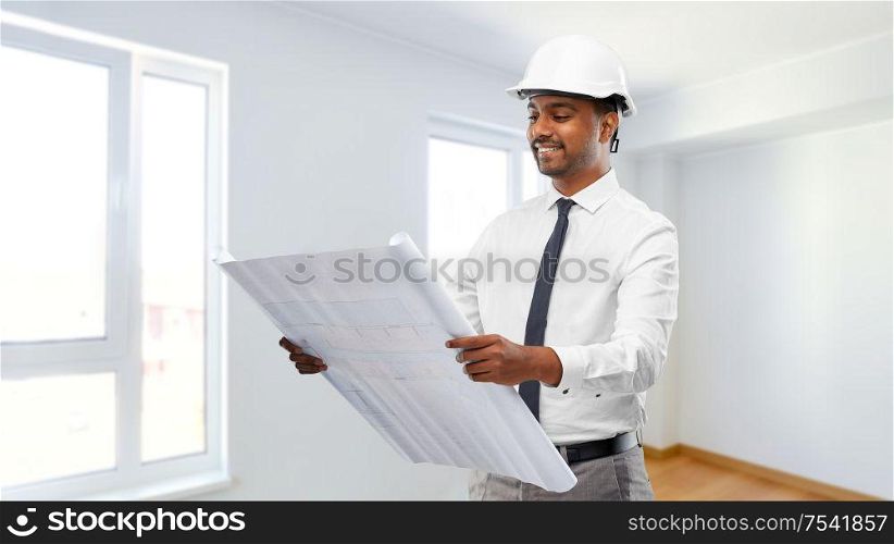 architecture, construction business and people concept - smiling indian male architect in helmet with blueprint over empty room at new home background. indian male architect in helmet with blueprint
