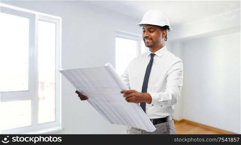 architecture, construction business and people concept - smiling indian male architect in helmet with blueprint over empty room at new home background. indian male architect in helmet with blueprint