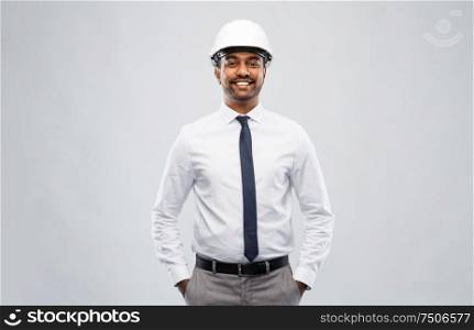 architecture, construction business and people concept - smiling indian male architect in helmet over grey background. indian male architect in helmet over grey