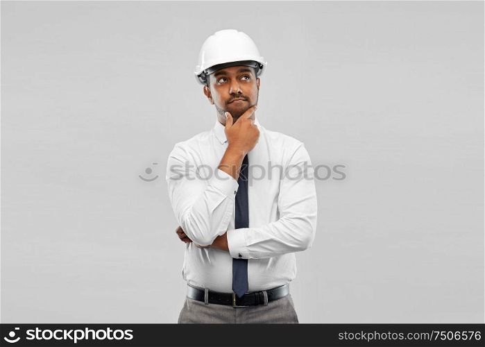 architecture, construction business and people concept - thinking indian male architect in helmet over grey background. indian male architect in helmet over grey