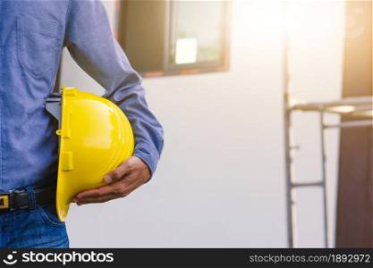 Architecture Engineer holding hard hat on site building construction background