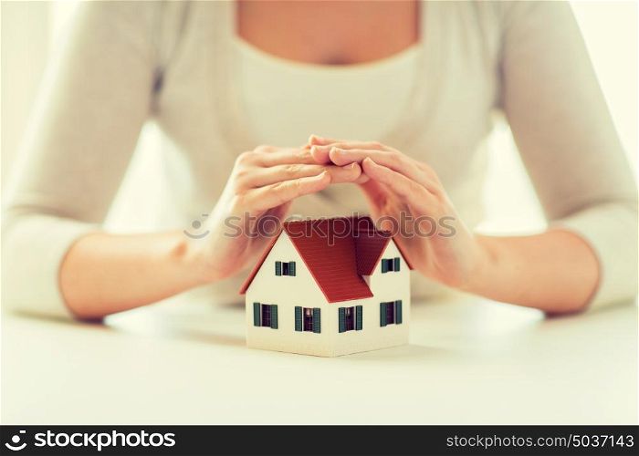 architecture, safety, security, real estate and property concept - close up of hands protecting house or home model. close up of hands protecting house or home model