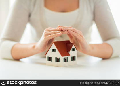 architecture, safety, security, real estate and property concept - close up of hands protecting house or home model