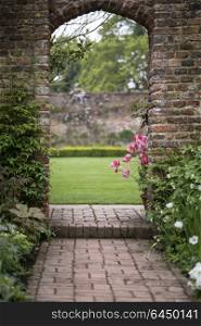 Archway in old English country garden landcape in Spring with tulips and border plants