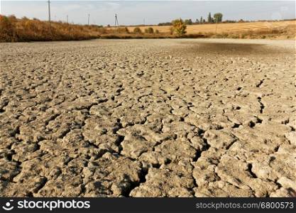Arid, dried and cracked soil of pond bottom, on the background autumn fields, bushes and trees