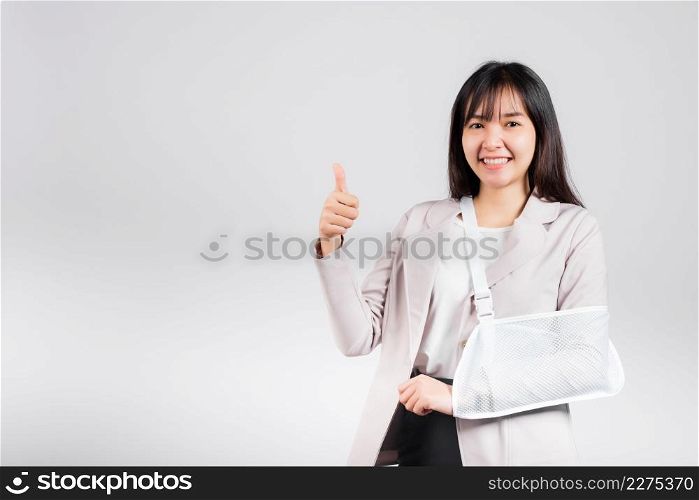 Arm broken. Business woman confident smile broken after accident wear arm splint for treatment show thumb up finger for good sign, happy Asian female sling support hand isolated on white background