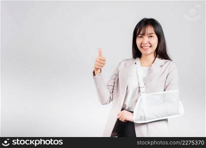 Arm broken. Business woman confident smile broken after accident wear arm splint for treatment show thumb up finger for good sign, happy Asian female sling support hand isolated on white background