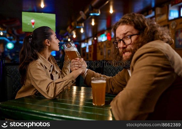 Arm wrestling challenge between man and woman at pub. Happy friends fighting at sport bar. Woman drinking beer and winning guy. Arm wrestling challenge between man and woman at pub