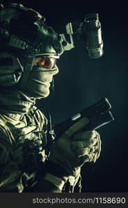 Army elite commando, professional mercenary, counter-terrorist tactical team fighter in combat helmet, equipped night-vision device, creeping in darkness with service pistol in hand, studio shoot. Elite commando soldier sneaking with pistol in hand