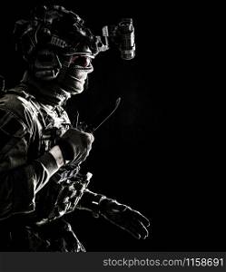 Army elite commando, professional mercenary, counter-terrorist tactical team fighter in combat helmet, equipped night-vision device, creeping in darkness with service knife in hand, studio shoot. Elite commando soldier sneaking with knife in hand
