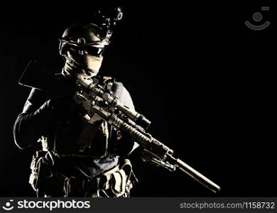 Army elite troops marksman, special operations forces sniper wearing mask and glasses, night-vision or infrared thermal imaging device on helmet, holding service rifle with optical sight and silencer. Army marksman with sniper rifle in darkness