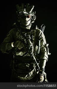 Army elite troops serviceman, counter-terrorist team member wearing mask and glasses, equipped night-vision device, radio headset mounted on combat helmet, armed submachine gun, standing in darkness. Army elite troops serviceman standing in darkness