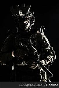Army elite troops serviceman, counter-terrorist team member wearing mask and glasses, equipped night-vision device, radio headset mounted on combat helmet, armed submachine gun, standing in darkness. Army elite troops serviceman standing in darkness