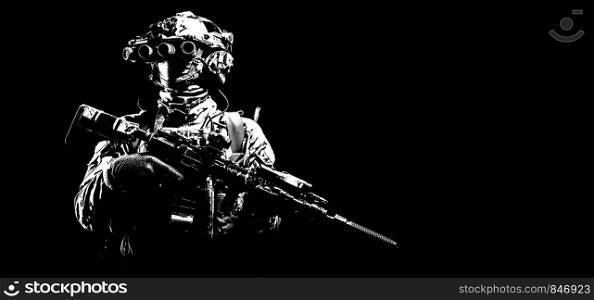Army infantry in battle uniform, armed assault rifle with laser sight and silencer, standing in darkness, looking through night vision goggles, low key half length, studio portrait on black background. Modern combatant wearing night vision device black background