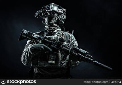 Army infantry in battle uniform, armed assault rifle with laser sight and silencer, standing in darkness, looking through night vision goggles, low key half length, studio portrait on black background. Modern combatant wearing night vision device black background