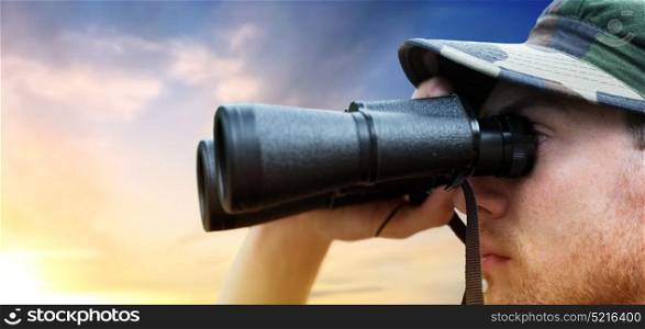 army, military service and people concept - close up of young soldier, ranger or hunter with binocular looking at something over sky background. close up of soldier face looking to binocular