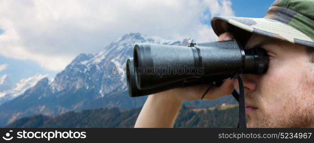 army, military service and people concept - close up of young soldier, ranger or hunter with binocular looking at something over mountains background. close up of soldier face looking to binocular