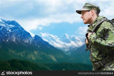 army, military service and people concept - young soldier or traveler in camouflage uniform with backpack hiking over mountains background. soldier in military uniform with backpack hiking