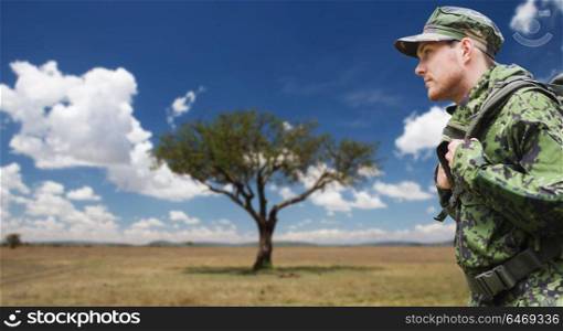 army, military service and people concept - young soldier or traveler in camouflage uniform with backpack hiking over savannah background. soldier in military uniform with backpack hiking