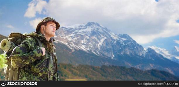 army, military service, travel and tourism concept - young soldier or traveler in camouflage uniform with backpack hiking over mountains background. soldier in military uniform with backpack hiking