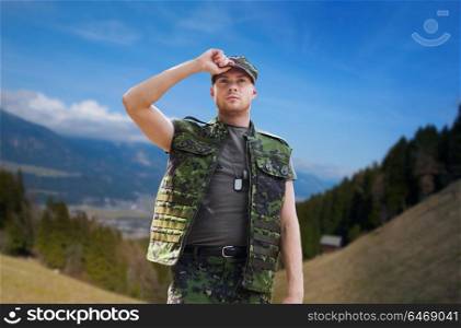 army, national service and people concept - young soldier or ranger wearing military uniform over mountains background. soldier in military uniform outdoors