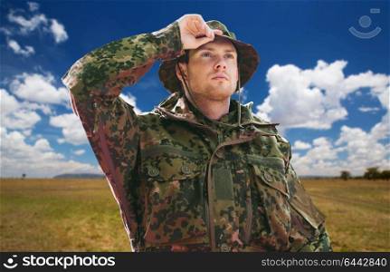 army, national service and travel concept - young soldier, ranger or traveler wearing military uniform and jungle hat over natural background and blue sky. soldier or traveler in military uniform over sky