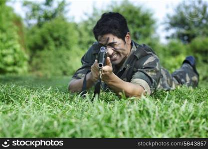 Army soldier aiming with rifle while lying on grass