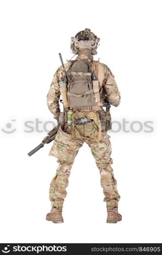 Army soldier in camo uniform and battle helmet, equipped tactical radio station with headset, wearing backpack, carrying ammo, rope, grenades in waist pouch, standing backwards isolated studio shoot. Armed army soldier standing backwards studio shoot