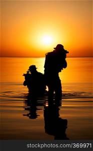 Army soldiers with rifles orange sunset silhouette in action during raid crossing river in the water. Army soldier silhouette