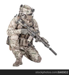 Army special forces infantry in battle uniform, radio headset on helmet, armed service rifle, standing on knee, waiting in ambush, patrolling area, observing territory studio shoot isolated on white. Soldier with rifle standing on knee studio shoot