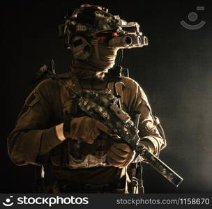 Army special forces tactical group fighter moving in darkness, using radio headset, looking through four lens night-vision, thermal imaging device on helmet, armed small submachine gun with silencer. Army special forces tactical group fighter in dark