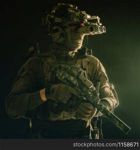 Army special forces tactical group fighter moving in darkness, using radio headset, looking through four lens night-vision, thermal imaging device on helmet, armed small submachine gun with silencer. Army special forces tactical group fighter in dark