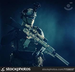 Army special operations soldier, counter-terrorist crew sniper, marksman in combat helmet, hiding face behind mask, armored service rifle with optical sight, low key studio shoot on blue background. Counter terrorist squad sniper soldier studio shoot
