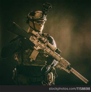Army special operations soldier, counter-terrorist crew sniper, marksman in combat helmet, hiding face behind mask, armored service rifle with optical sight, low key studio shoot on blue background. Counter terrorist squad sniper soldier studio shoot
