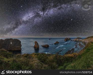 Arnia Beach (Spain) Atlantic Ocean coastline night view from rocky stones. And starry Milky Way in sky.