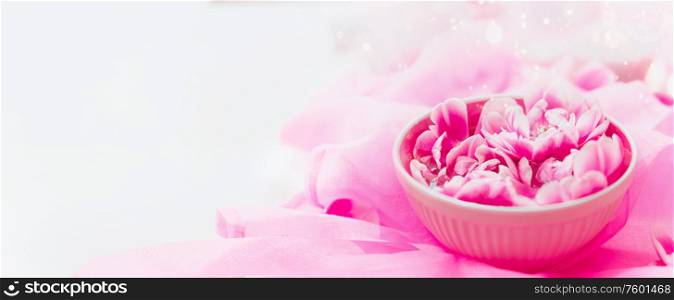 Aroma water bowl with pink flowers at light silk background. Spa and wellness composition. Banner. Essential water .